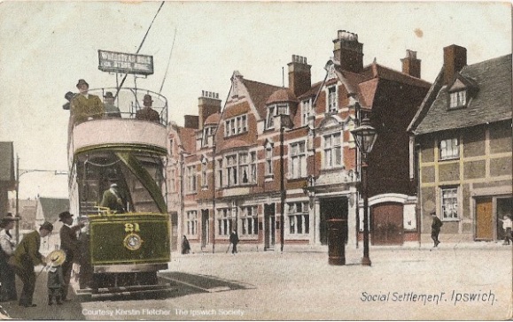 A colourised photo with a three storey brick building in the background and a double-decker green electric tram in the foreground.