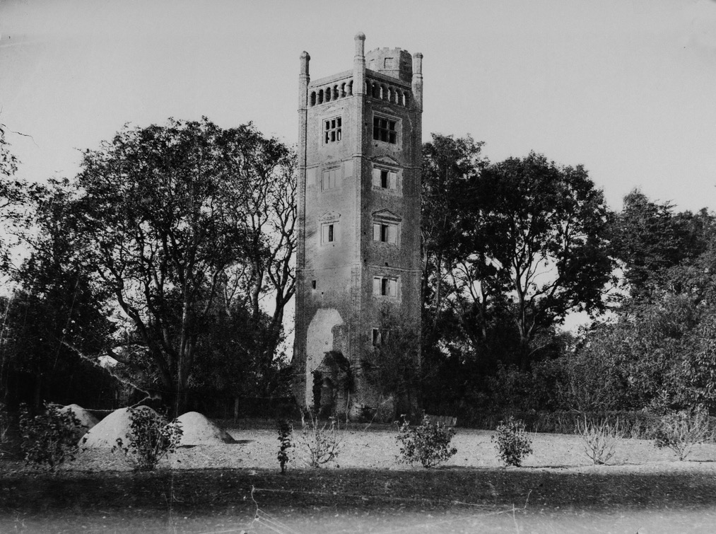 A photo of a seven-storey square brick tower with one window on each side per floor. There are trees around it, almost as tall as the tower.