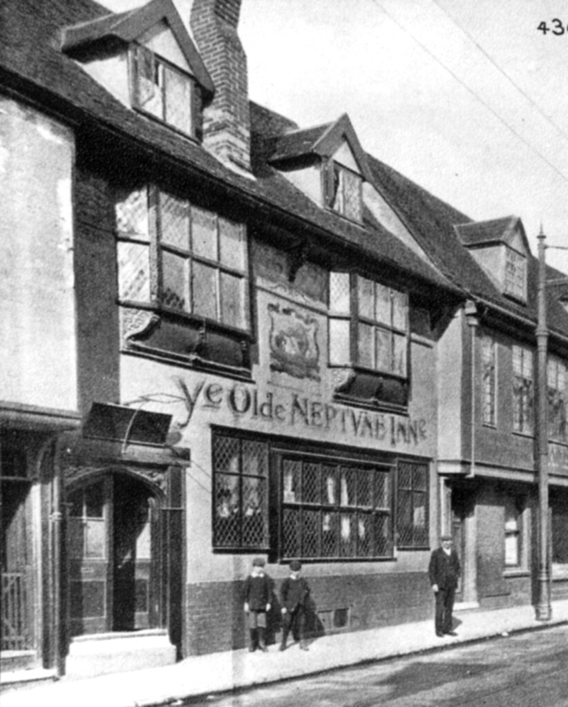 A photo of a very old building with 'Ye Olde Neptune Inn' painted on the front. It has leaded windows, a tall brick chimney. Two small boys and a man stand on the pavement in front.