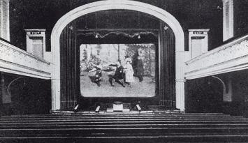 A photo of a cinema auditorium looking over the seats directly at the screen. There are balconies on either side.