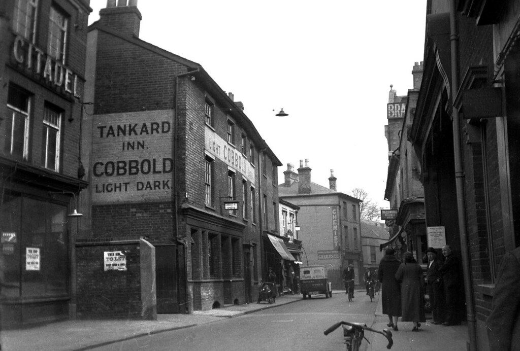 A photo of a street with mainly three-storey brick buildings. The main one has a big sign painted on one end reading 'Tannkard Inn. Cobbold Light Dark.' We can see the edge of the building at the far left and part of a big sign reading 'CITADEL'.